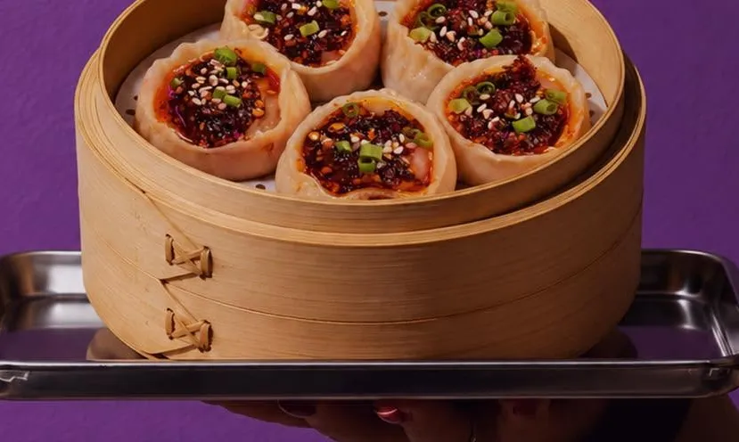 Steamer of chicken dumplings topped with chili oil and sesame.