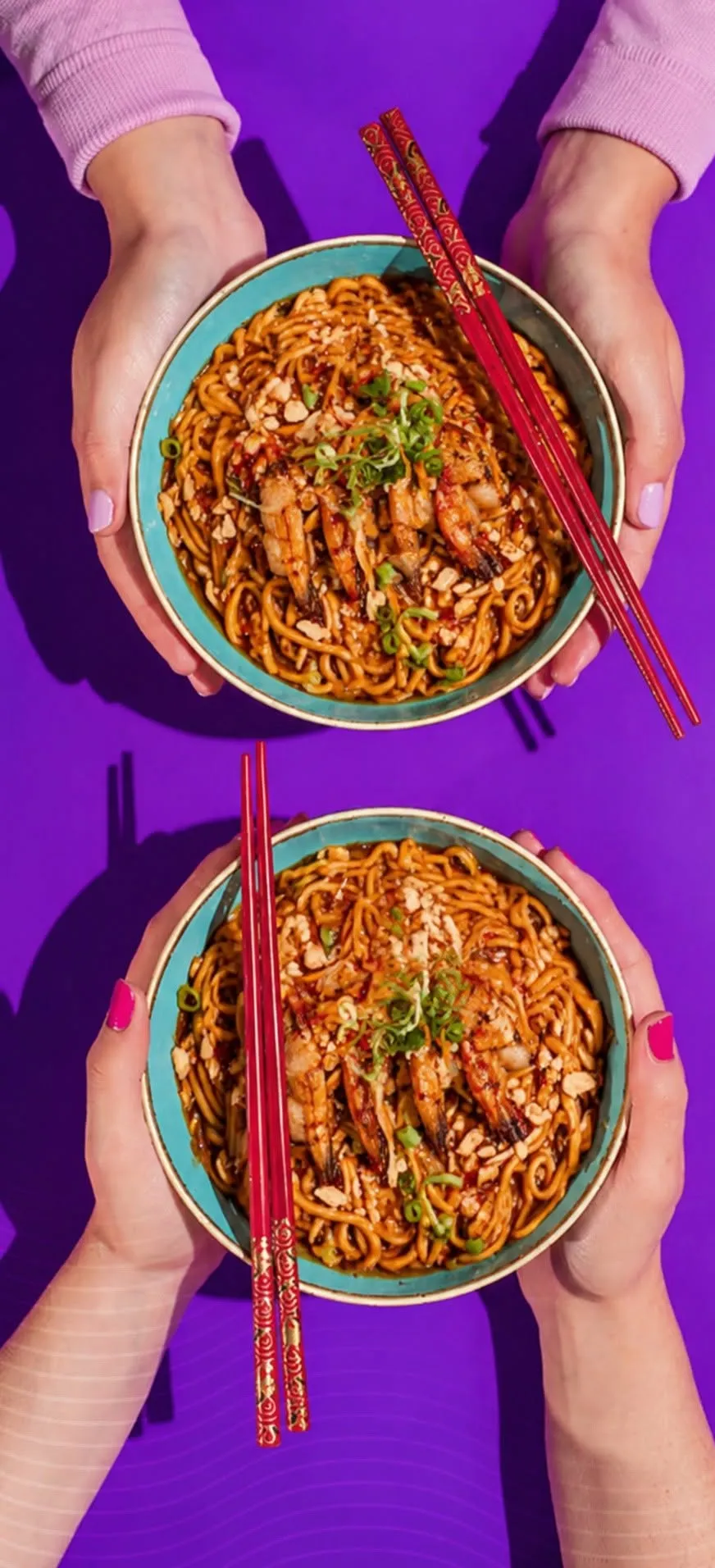 Two pairs of hands holding bowls of peanut noodles with red chopsticks.
