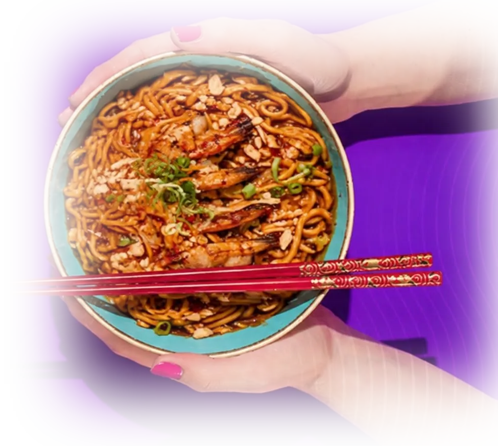 A second pair of hands holding a matching bowl of noodles, seen from above.