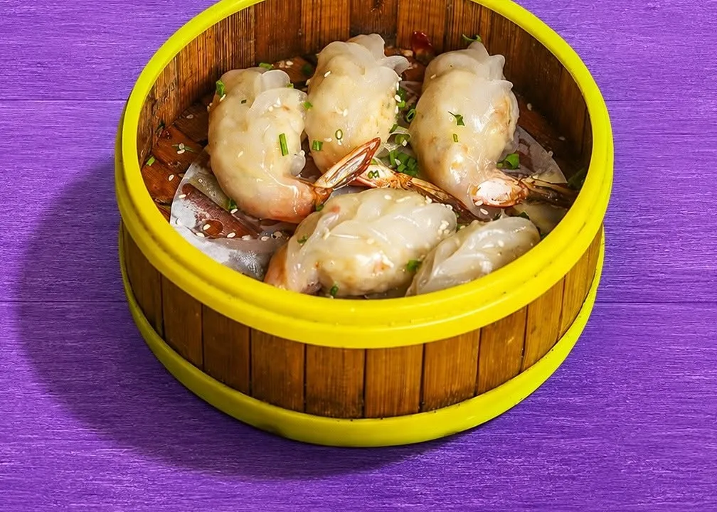 Jumbo prawn dumplings with the prawn tails showing, in a yellow-rimmed steamer.