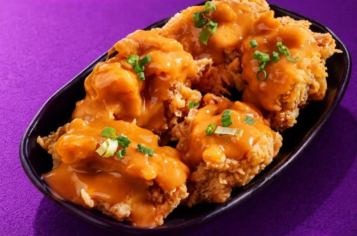 Crispy chicken thighs covered in nanban sauce and spring onion on a black plate.