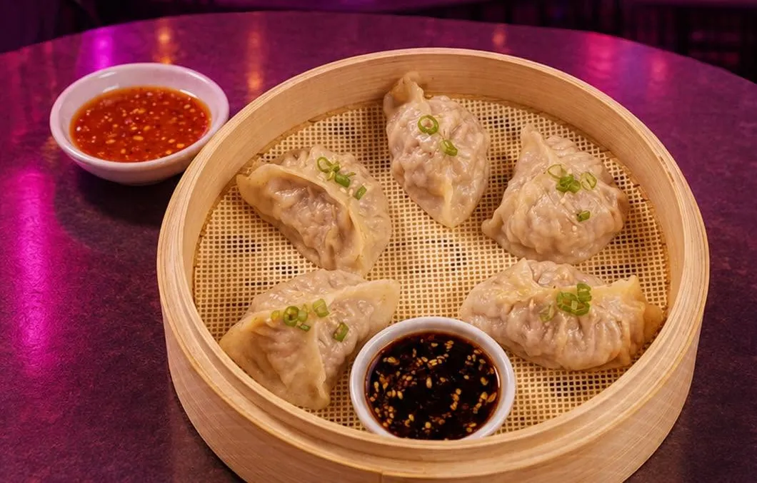 Steamed chicken dumplings in a bamboo steamer with dipping sauces.
