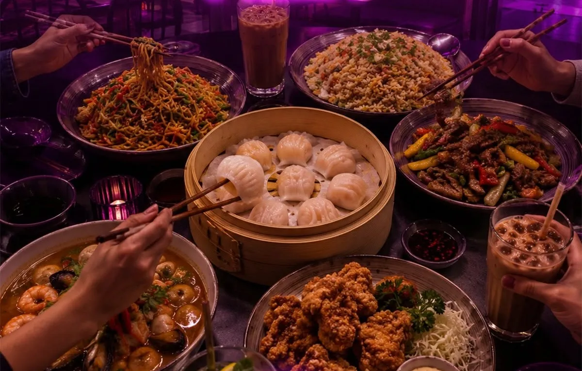 A table crowded with noodles, fried rice, dumplings and drinks, with hands reaching in with chopsticks.